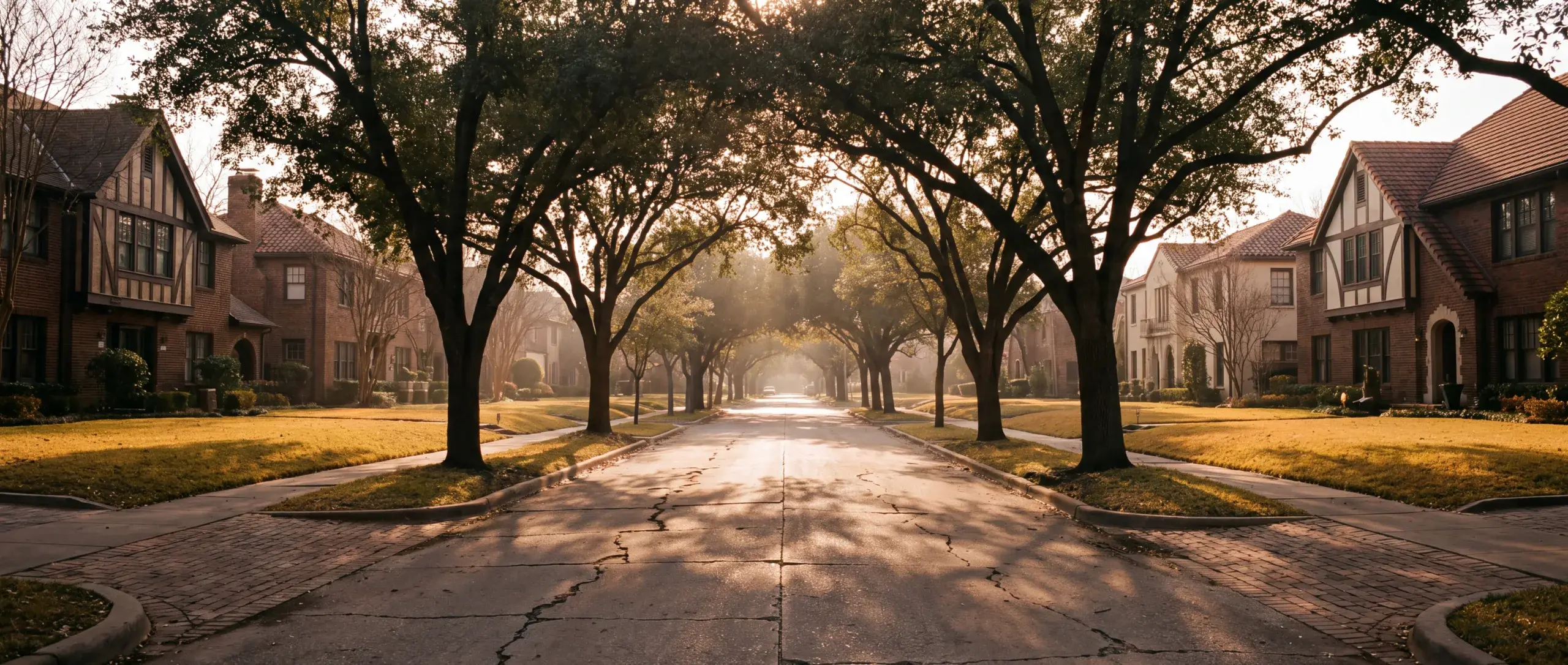 A tree-lined East Dallas street of 1930s Tudor and Spanish revival homes at golden hour.